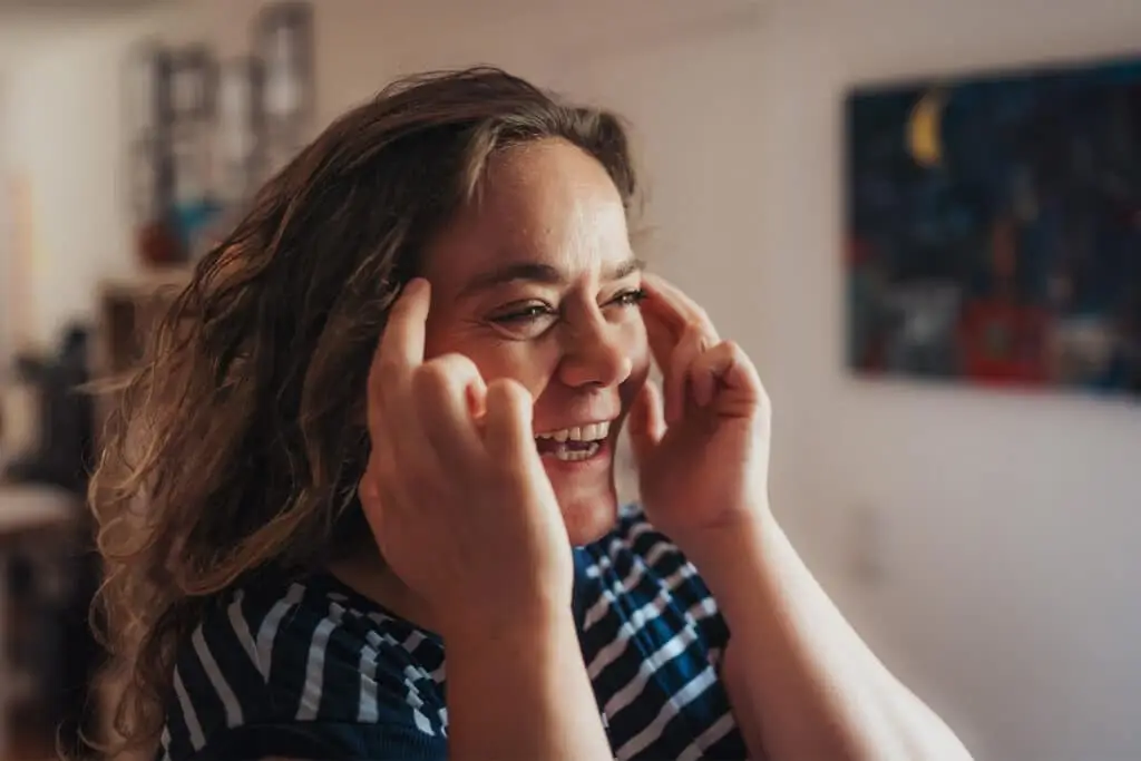Claudia lachend mit Fingern an ihrer Schläfe