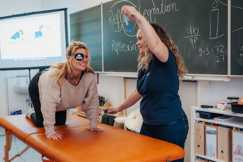 Zwei Frauen bei einer Reflexintegrationseinheit: Eine befindet sich im Vierfรผรlerstand mit Augenklappe, die andere fรผhrt eine gezielte visuelle Reizung mit einem Objekt durch.
Claudia Hannemann, Grรผnderin der Awesome Academy, leitet das Reflexintegrationstraining an.